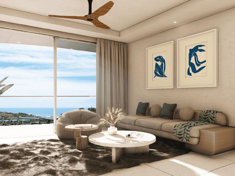 A bright, modern living room featuring large sliding glass doors that open to a scenic coastal view, complemented by a ceiling fan and tiled floors.