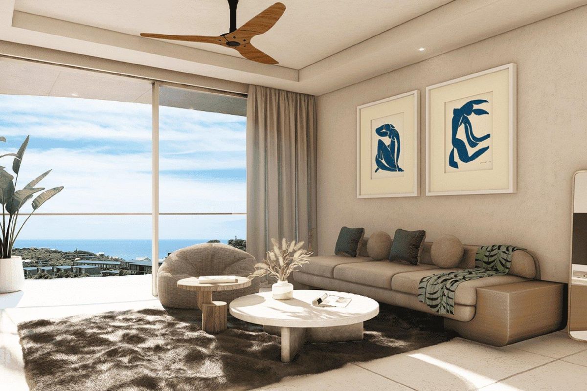 A bright, modern living room featuring large sliding glass doors that open to a scenic coastal view, complemented by a ceiling fan and tiled floors.