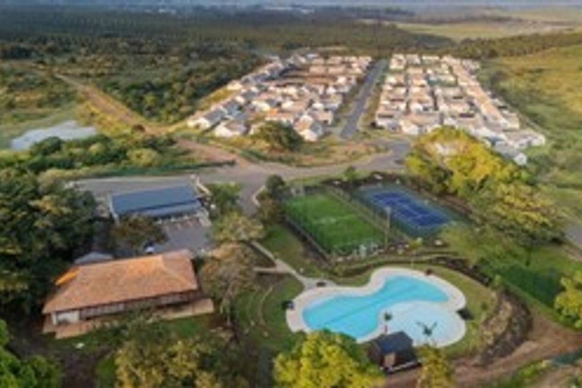 Aerial view of a residential estate featuring a swimming pool, sports facilities, clubhouse, and surrounding landscaped green space.
