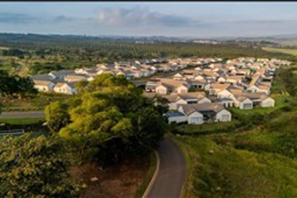 An aerial view of a residential housing estate surrounded by lush green landscape and a paved access road.