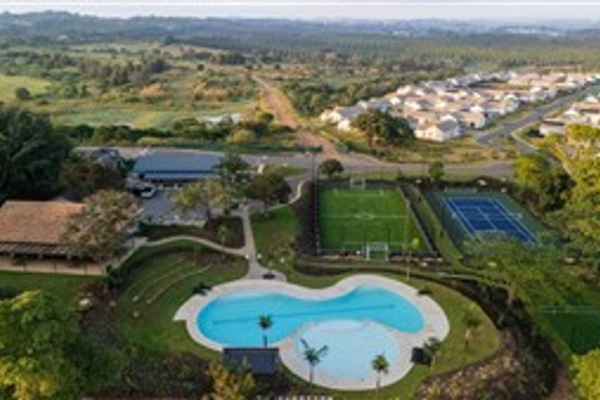 Aerial view of the residential estate featuring a swimming pool, tennis court, soccer field, and clubhouse facilities surrounded by landscaped grounds.