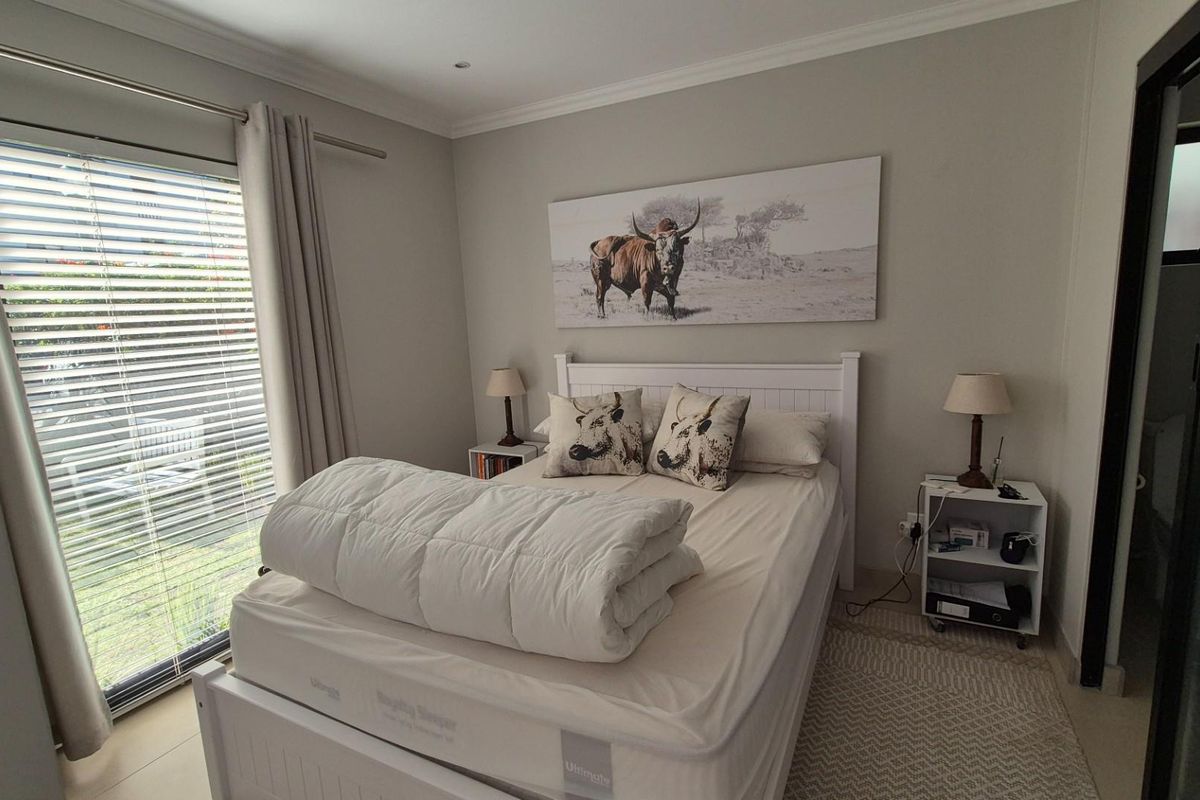A well-maintained bedroom featuring neutral wall tones, tiled flooring, and a large sliding glass door with venetian blinds providing natural light.