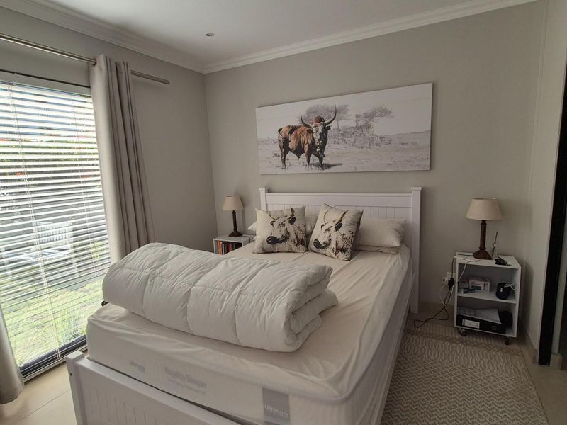 A well-maintained bedroom featuring neutral wall tones, tiled flooring, and a large sliding glass door with venetian blinds providing natural light.