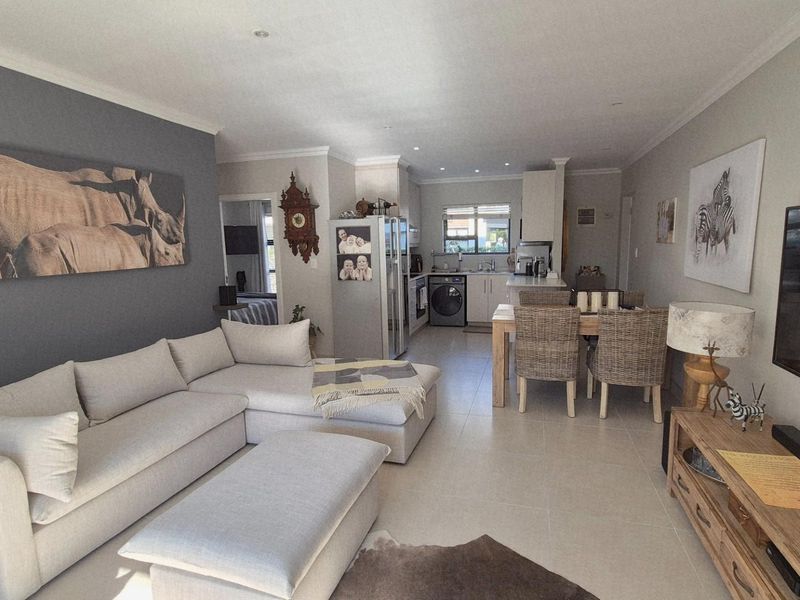 An open-plan living and dining area featuring tiled floors, recessed lighting, and a functional kitchen with built-in appliances.