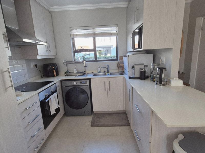 A well-maintained kitchen featuring light wood-grain cabinetry, stone countertops, a built-in oven, electric hob, and integrated laundry appliance space.