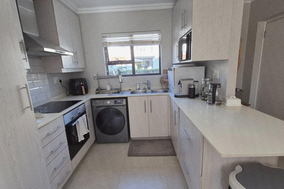 A well-maintained kitchen featuring light wood-grain cabinetry, stone countertops, a built-in oven, electric hob, and integrated laundry appliance space.