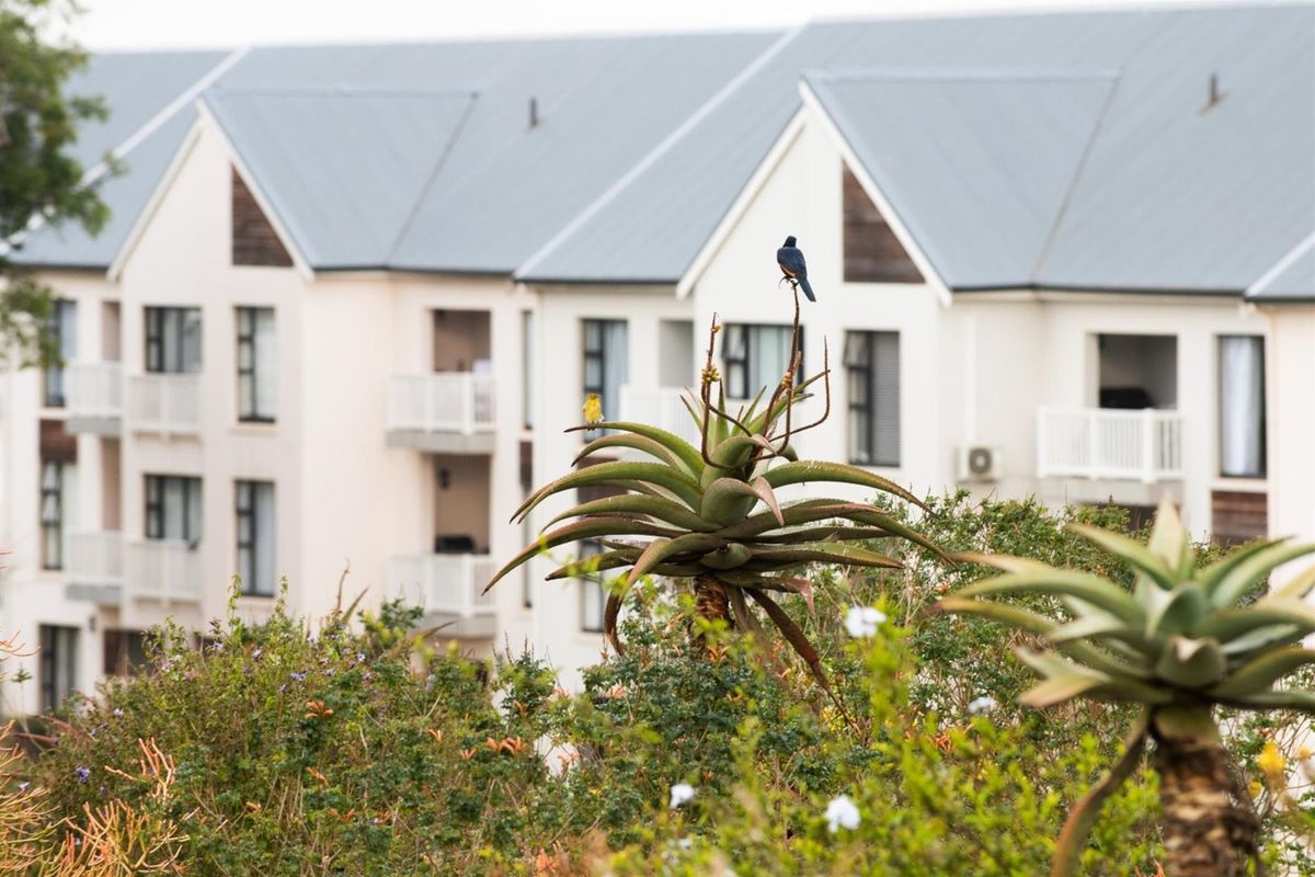 A view of the apartment complex exterior featuring pitched roofs, balconies, and landscaped garden area in the foreground.