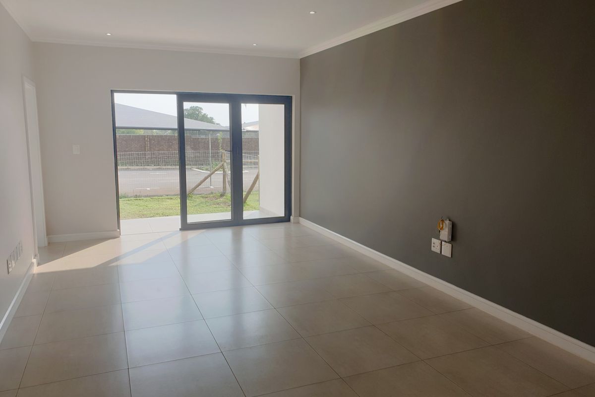 A bright, modern, and empty living room featuring neutral tiled flooring, a dark accent wall, and a large sliding glass door leading to the exterior.