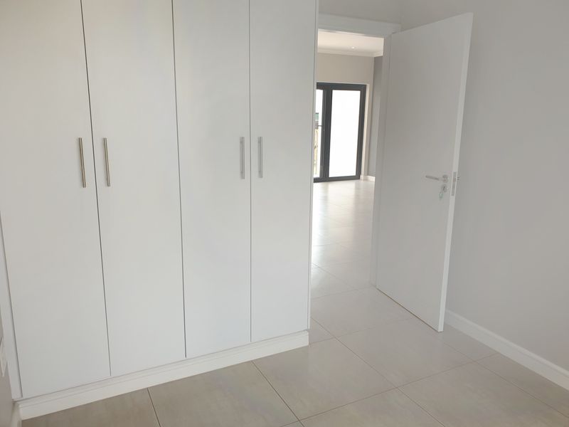 A bright, empty bedroom featuring modern built-in cupboards, neutral tiled flooring, and a clean, minimalist aesthetic.
