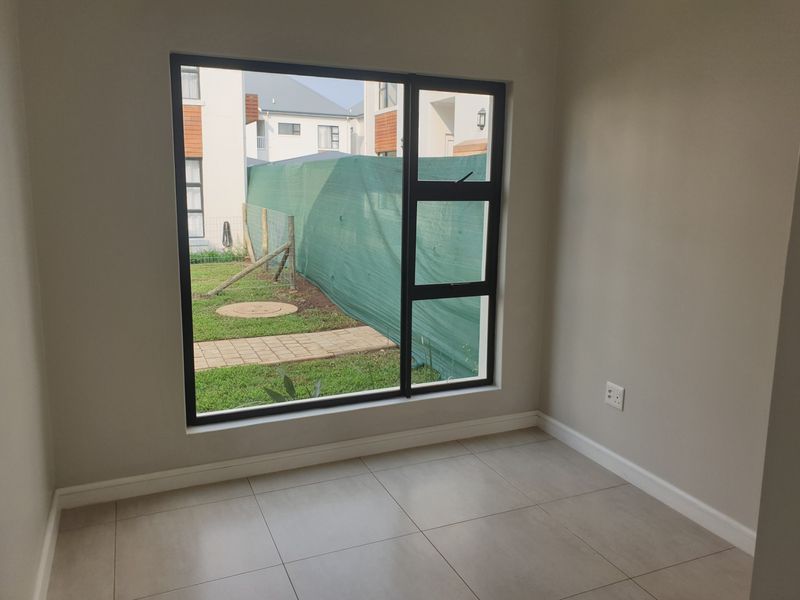 A bright, empty bedroom featuring modern tiled flooring, neutral walls, and a large aluminium-framed window overlooking the rear garden area.