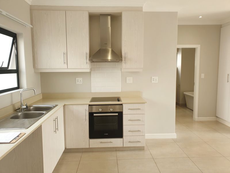 Modern kitchen featuring light wood-finish cabinetry, stainless steel appliances, electric hob, oven, and neutral tiled flooring with a clean subway tile backsplash.