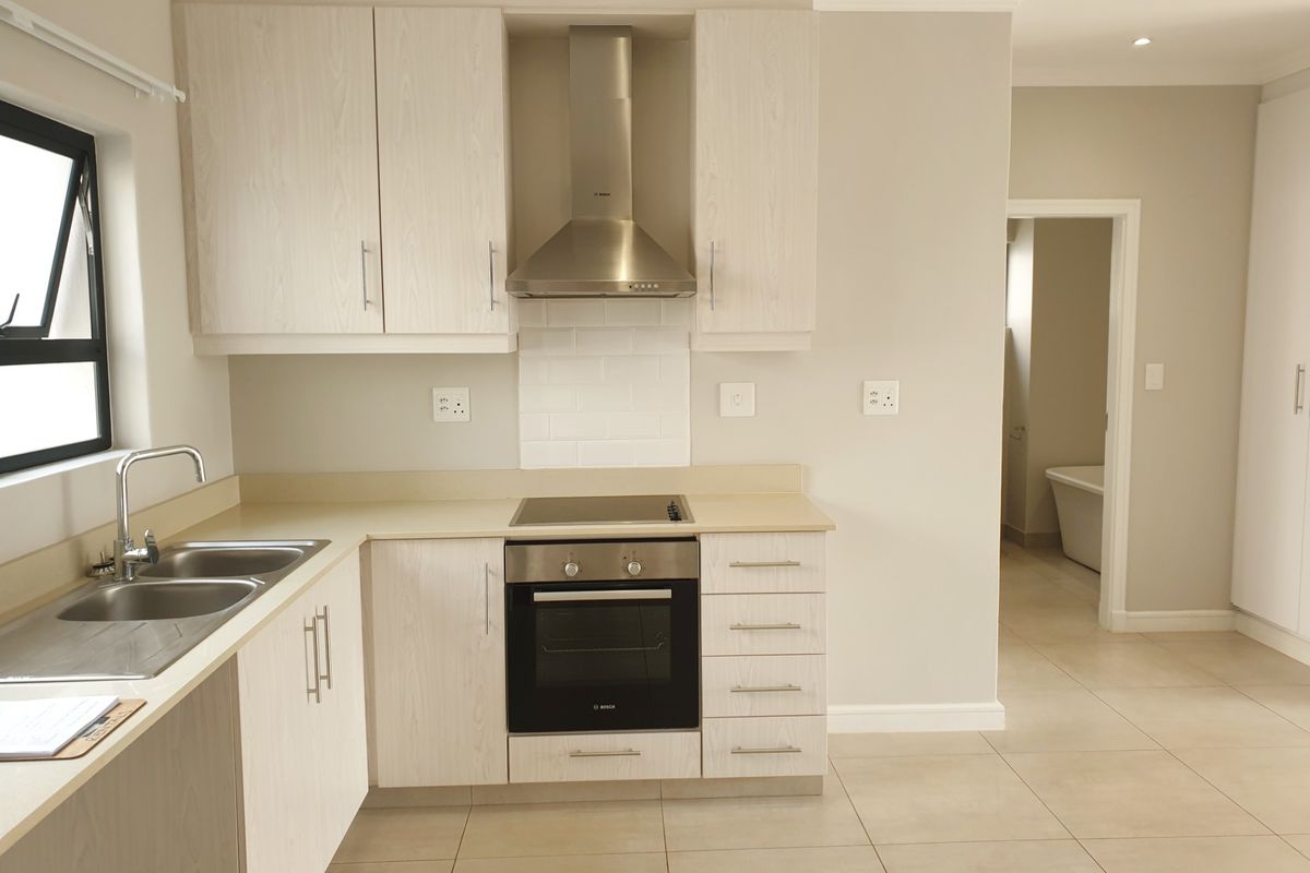 Modern kitchen featuring light wood-finish cabinetry, stainless steel appliances, electric hob, oven, and neutral tiled flooring with a clean subway tile backsplash.