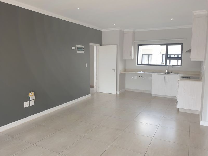 A bright and spacious open-plan living and kitchen area featuring neutral tiled floors, modern cabinetry, and a clean, contemporary finish throughout.