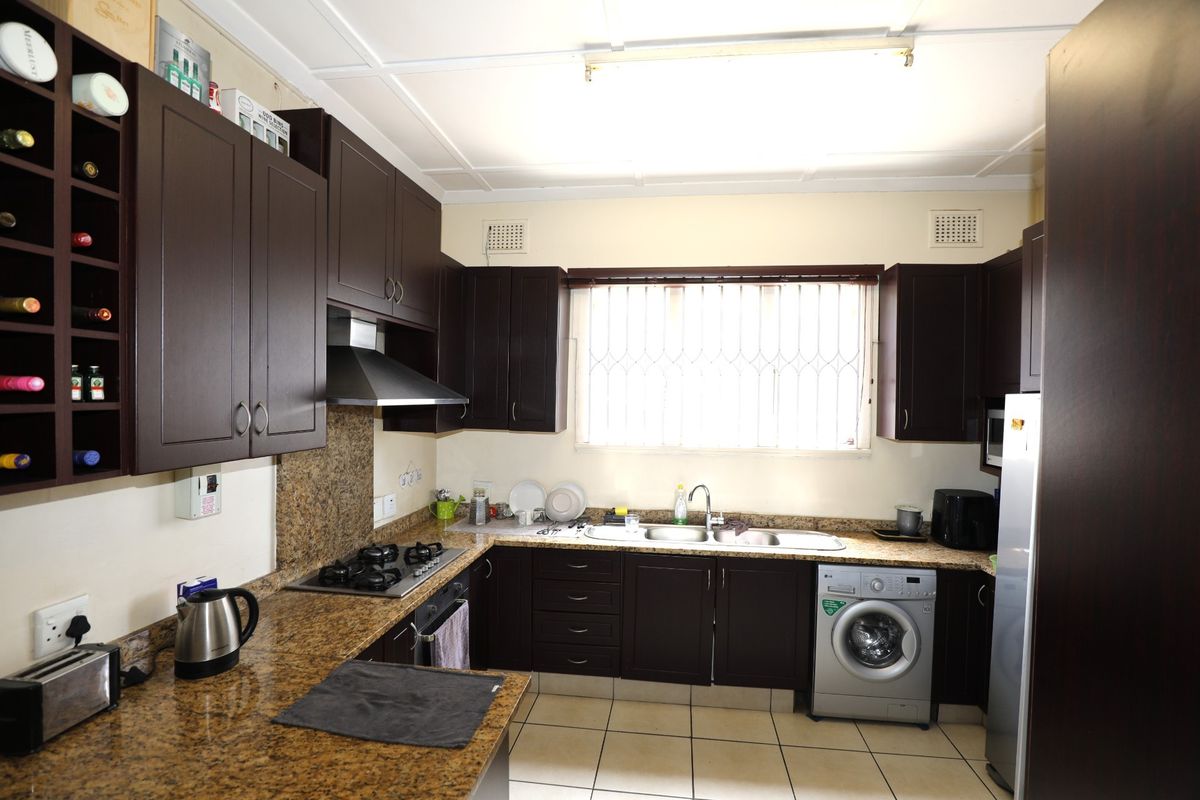 A functional kitchen featuring dark wood cabinetry, granite countertops, a built-in gas hob, stainless steel extractor fan, and integrated laundry appliance space.