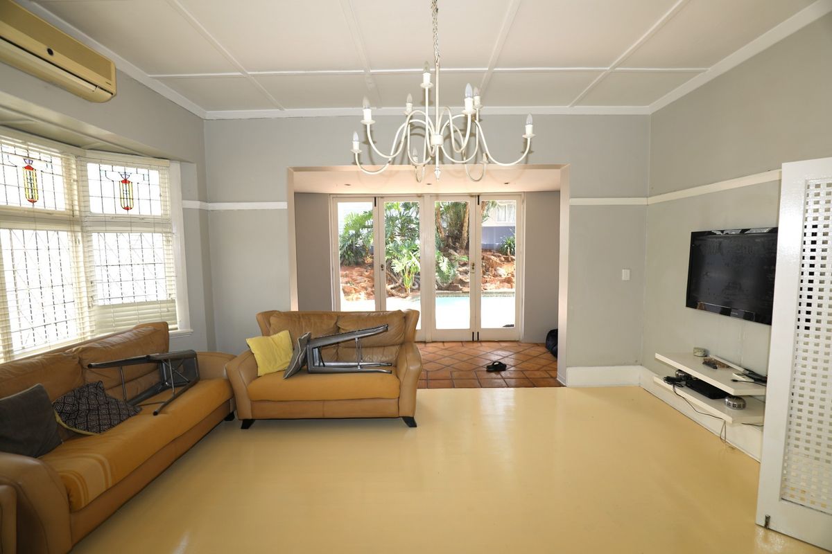 Spacious living room featuring a coffered ceiling, leaded glass bay windows, and direct access through glass doors to the outdoor pool area.