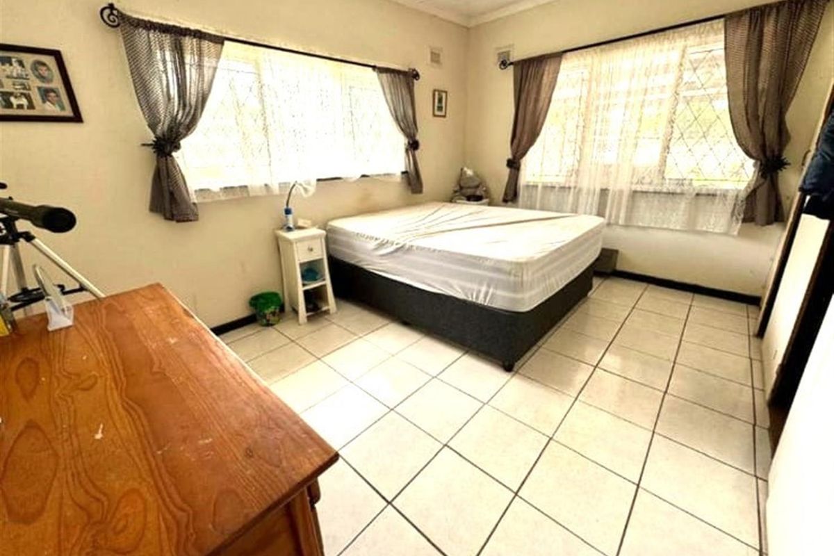 A bedroom featuring tiled flooring and large windows with security bars, offering a functional space ready for cosmetic updates.