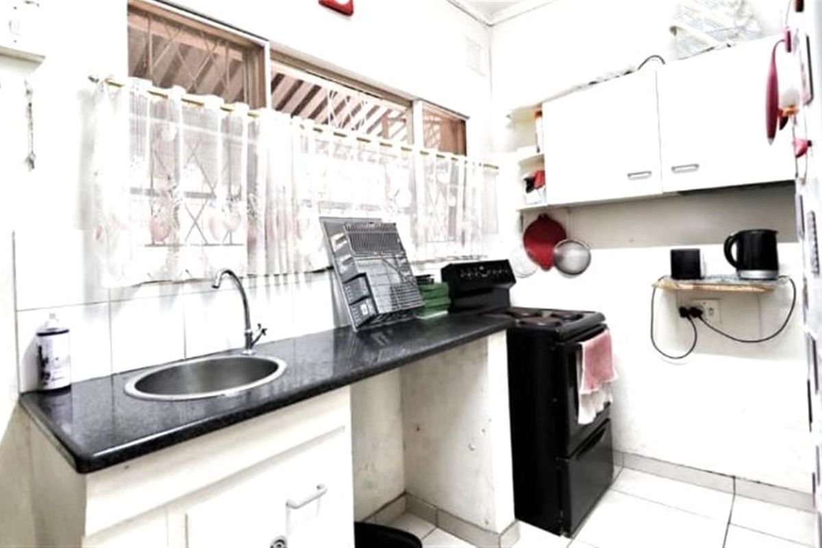 A compact kitchen featuring dark stone countertops, a stainless steel sink, and white cabinetry, providing a functional workspace with basic built-in fixtures.