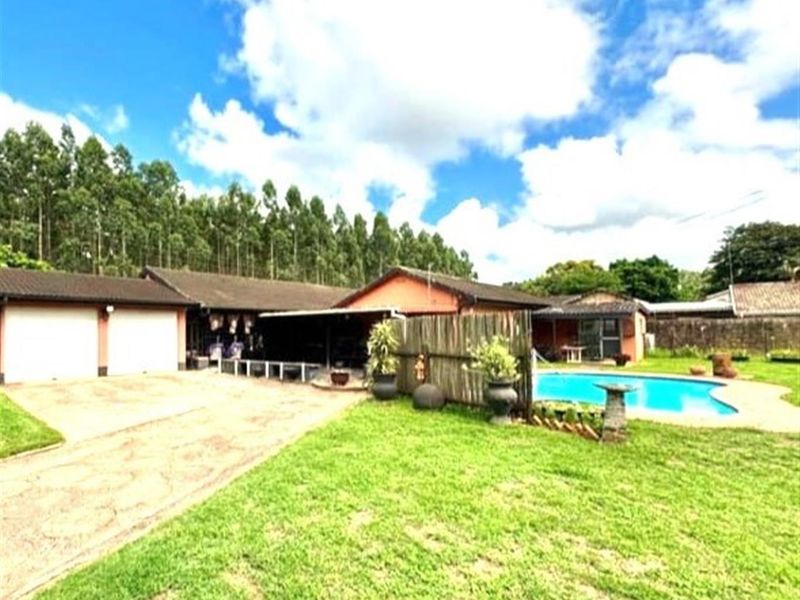 Spacious rear exterior featuring a swimming pool, paved driveway, double garage, and a covered patio area set within a large garden.