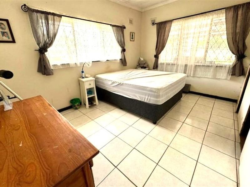 A bedroom featuring tiled flooring and large windows with security bars, offering a functional space ready for cosmetic updates.