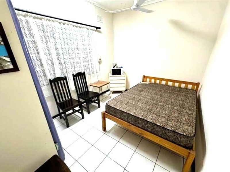 A simple bedroom featuring tiled flooring, a ceiling fan, and a window with curtain rod.