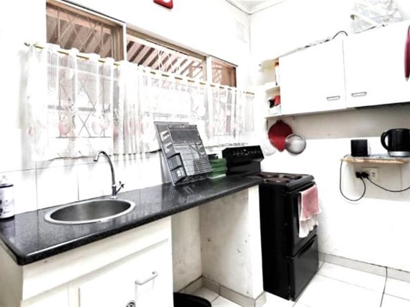 A compact kitchen featuring dark stone countertops, a stainless steel sink, and white cabinetry, providing a functional workspace with basic built-in fixtures.