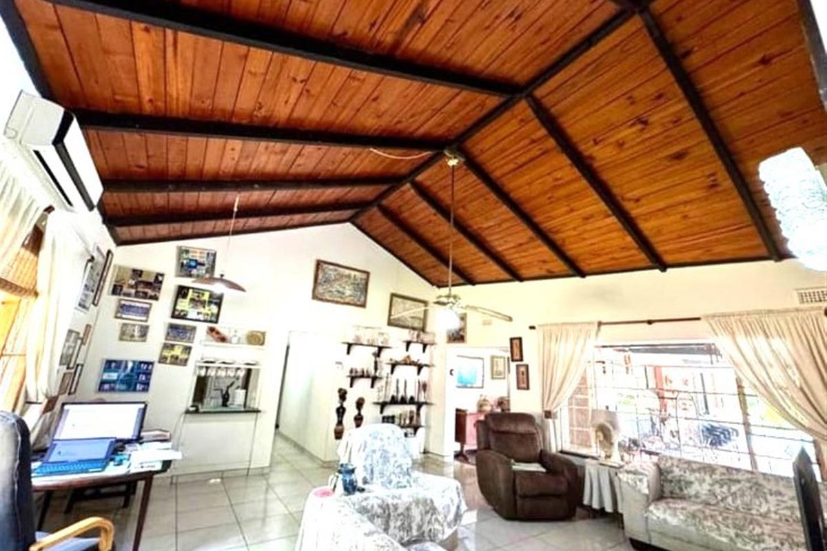 Spacious living area featuring a high vaulted timber-clad ceiling with exposed beams, tiled flooring, and a wall-mounted air conditioning unit.