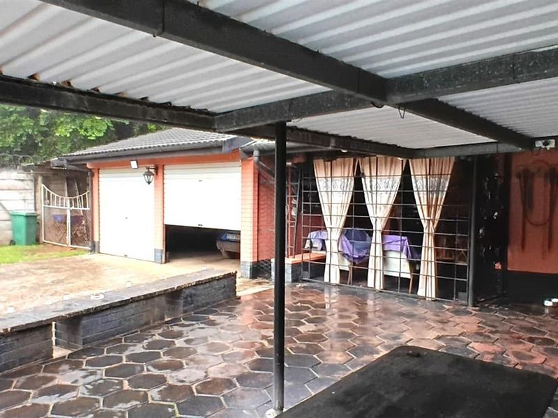 A covered outdoor patio area featuring paved flooring, adjacent to a brick garage structure with a double door entrance.
