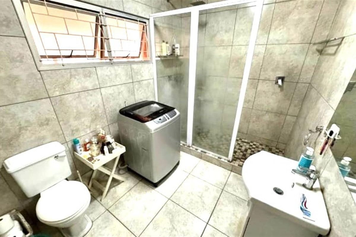A functional bathroom featuring a walk-in shower with glass enclosure, a pedestal basin, and a toilet, finished with neutral wall and floor tiling.