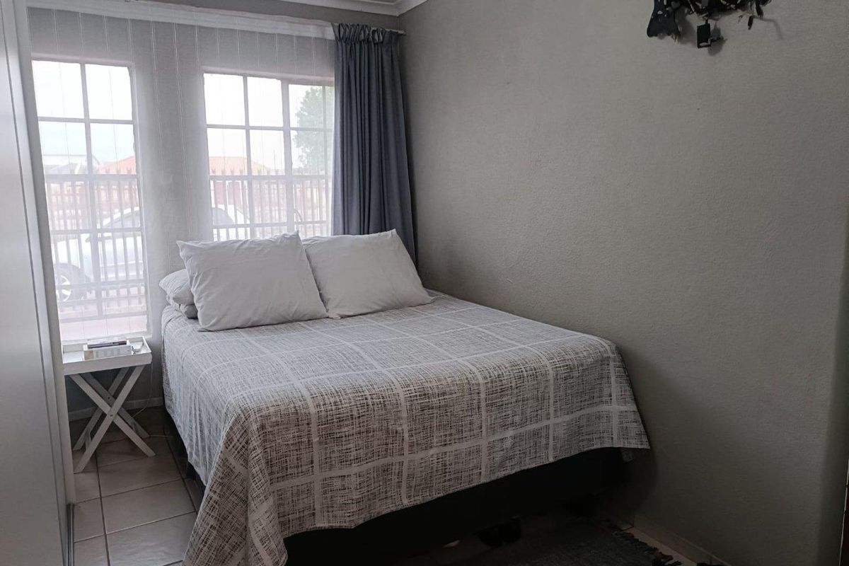 A functional bedroom featuring tiled flooring, neutral wall finishes, and natural light through a window with security bars.