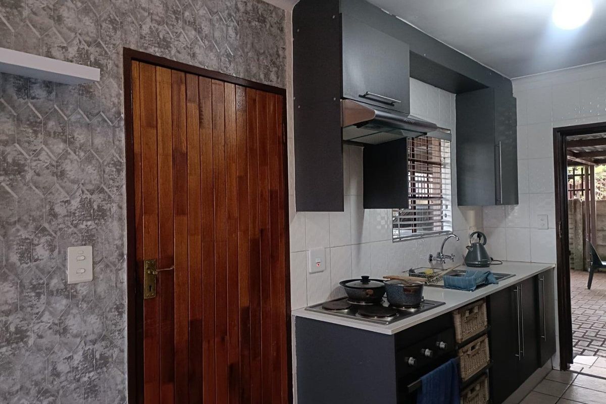 A functional kitchen featuring dark cabinetry, a built-in hob and oven, stainless steel sink, and a textured feature wall.