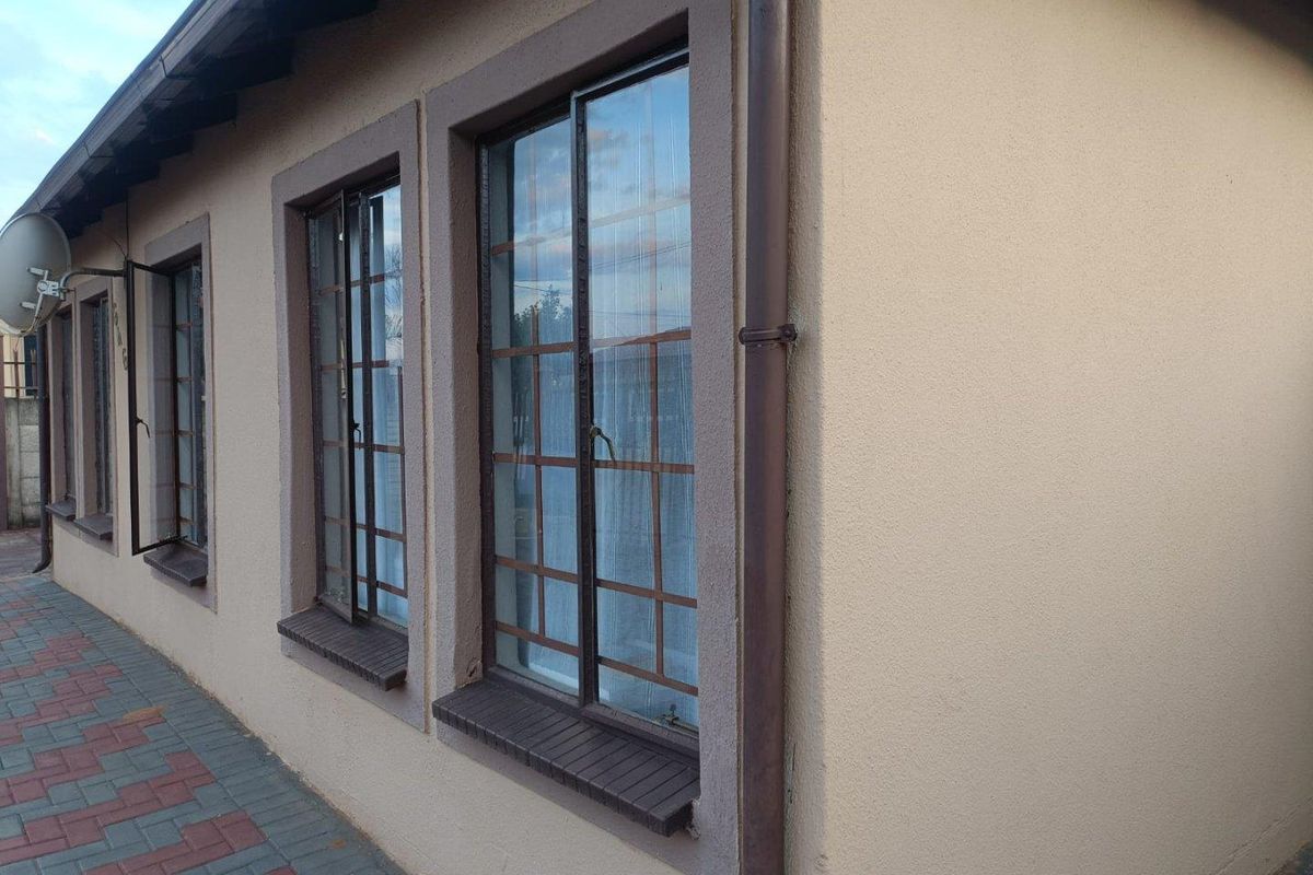 A side view of the property exterior featuring plastered walls, metal-framed windows, a downpipe, and a paved walkway.