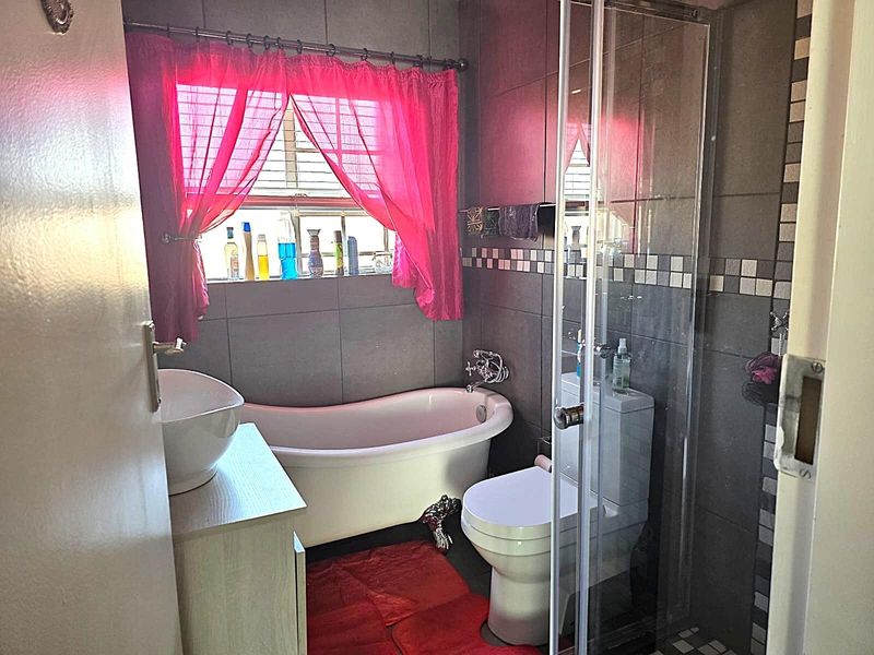 A compact bathroom featuring a freestanding bathtub, a separate glass-enclosed shower, a vanity basin, and a toilet with dark wall tiling.