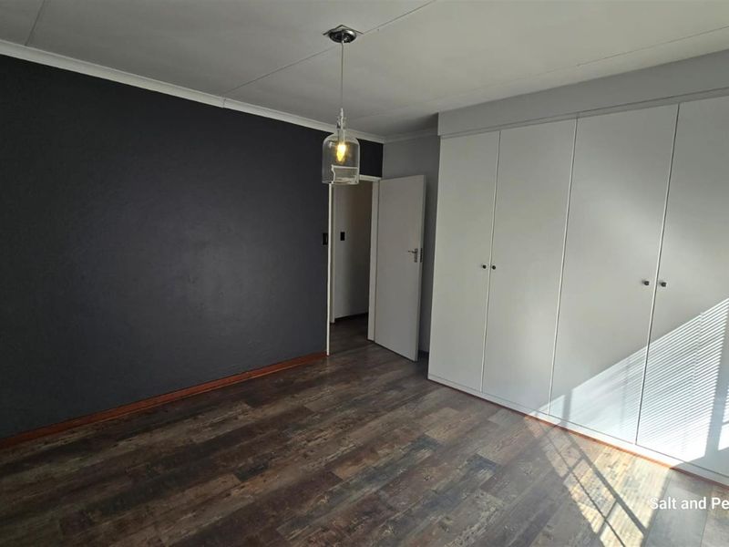 A bedroom featuring dark accent wall, wood-look flooring, and built-in white cabinetry with integrated storage.