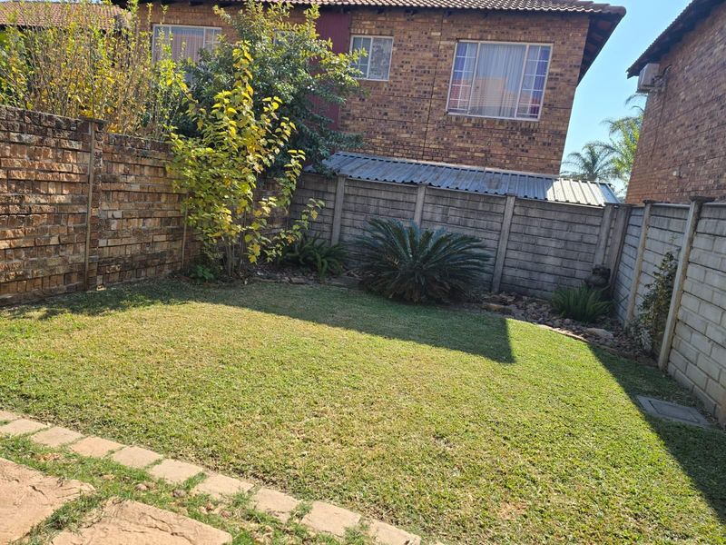 A private rear garden featuring a lawn area, established landscaping, and secure perimeter walling, providing a quiet outdoor space for the townhouse.