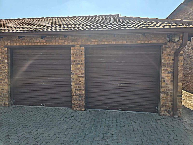 A double garage featuring brown roller shutter doors, brick facade construction, and a tiled roof, situated on a paved driveway.
