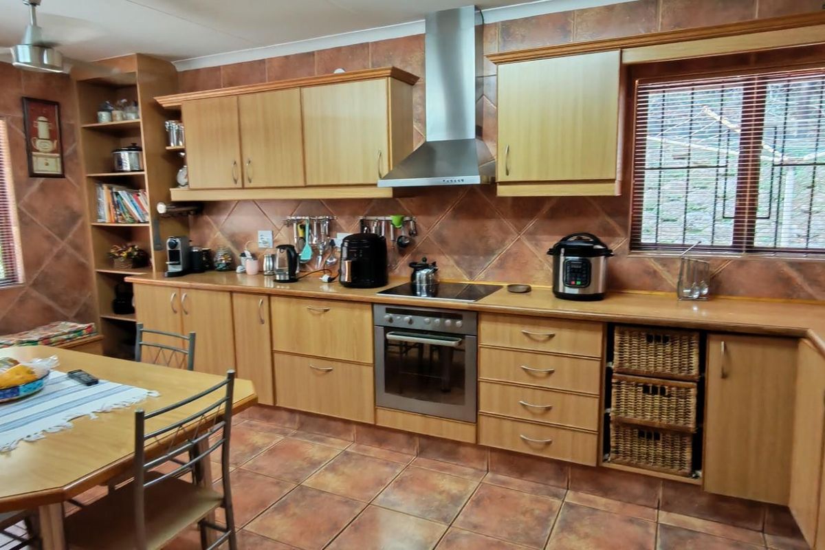 A functional kitchen featuring light wood cabinetry, tiled splashbacks, a built-in oven with extractor fan, and an integrated dining area.