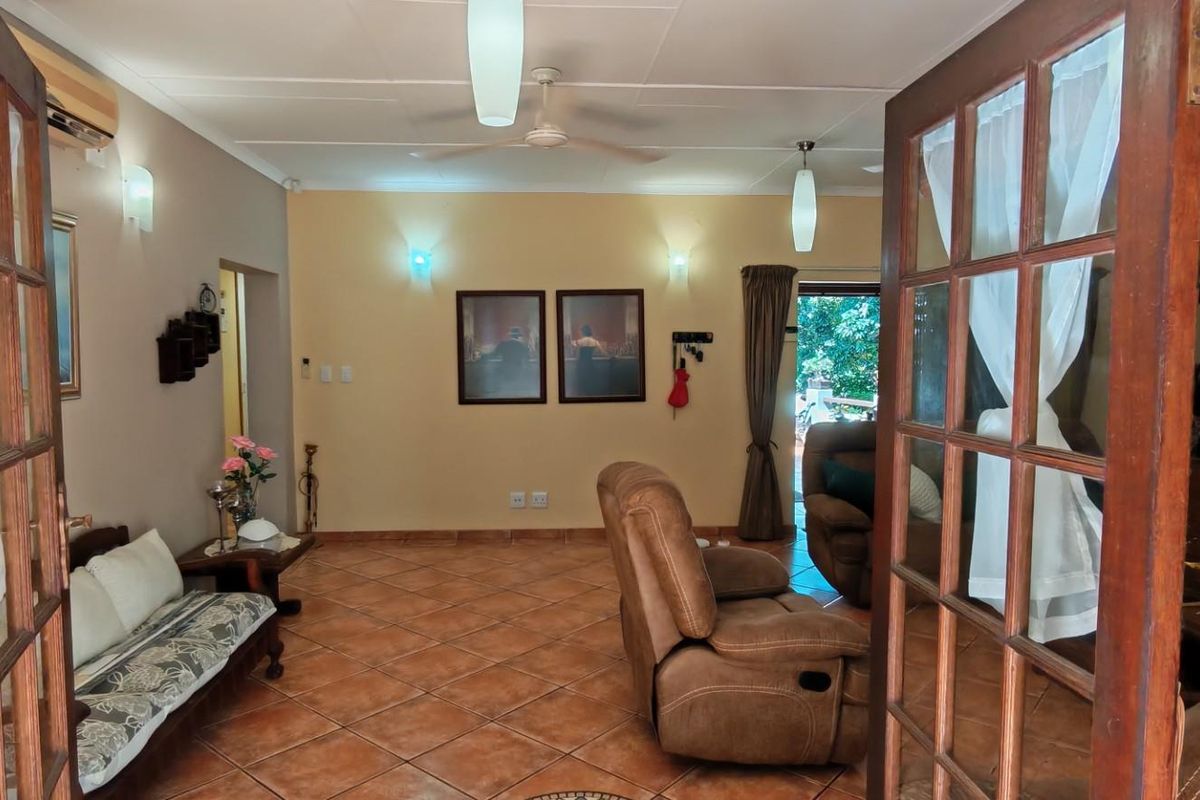 A living room featuring terracotta floor tiles, wooden French doors, and wall-mounted lighting fixtures, providing a warm and traditional atmosphere.