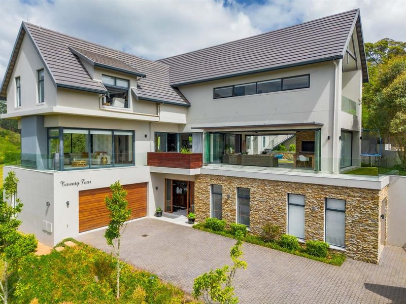 Modern multi-level residence featuring stone cladding, a paved driveway, double garage, and expansive glass stacking doors opening to a balcony.