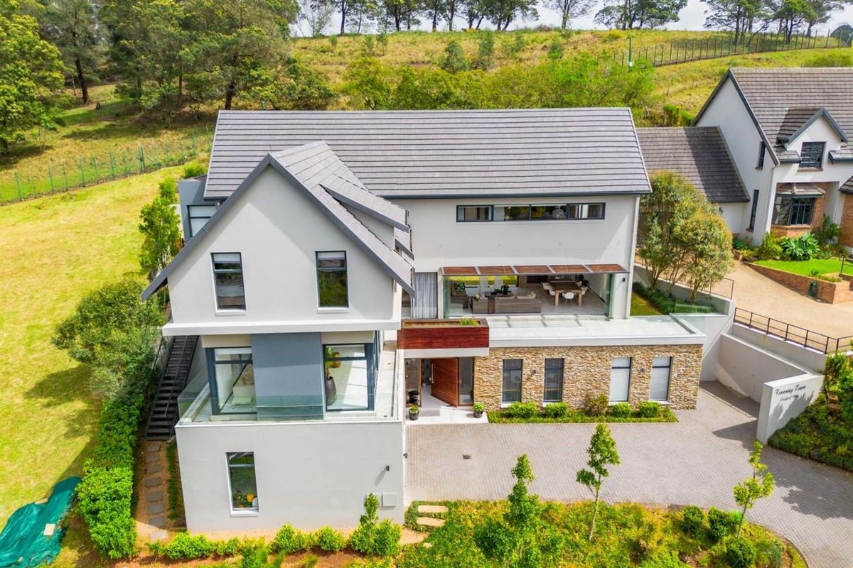 Aerial view of a modern multi-story residence featuring stone cladding, a paved driveway, and a spacious covered patio area set in a landscaped environment.