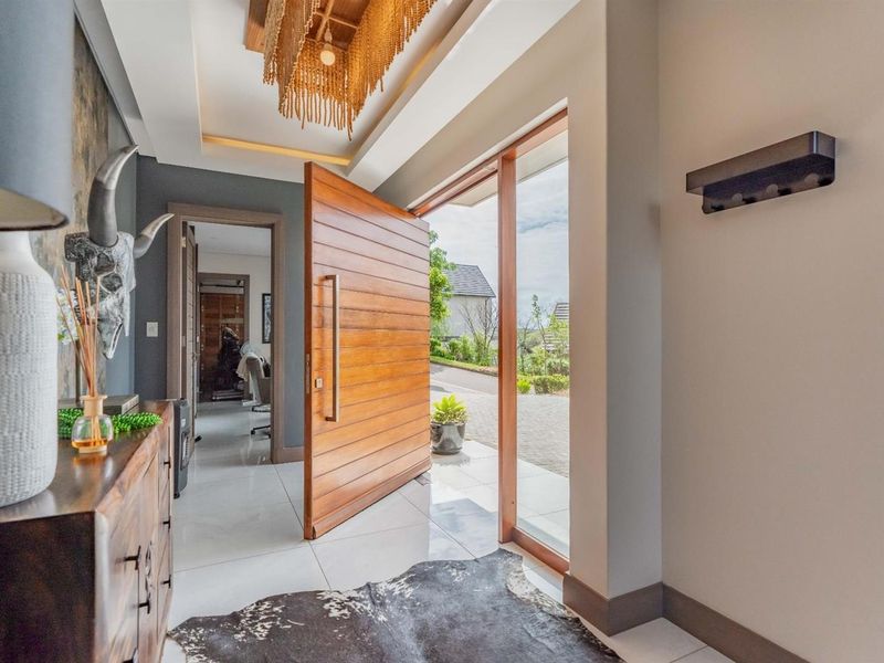 Modern entrance hall featuring a large timber pivot door, polished porcelain flooring, and elegant recessed ceiling lighting.