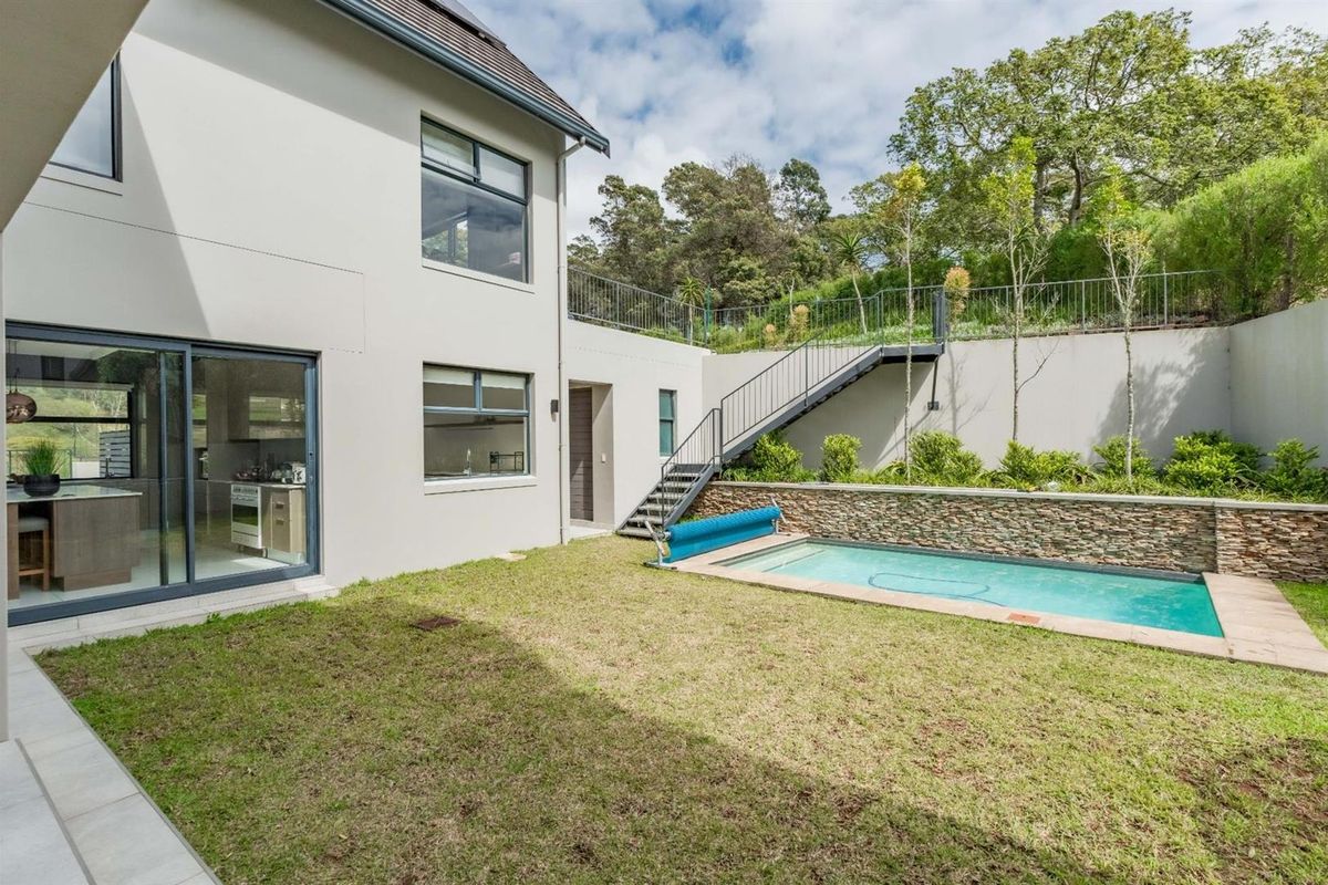 A well-maintained rear exterior featuring a swimming pool, stone-clad retaining wall, metal staircase, and a landscaped garden area.