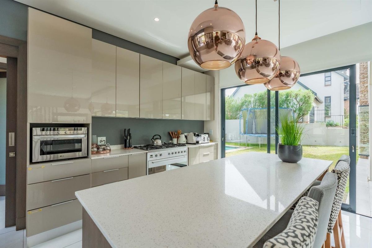 Modern kitchen featuring high-gloss cabinetry, stone countertops, a central island, and large sliding doors providing seamless access to the outdoor garden area.