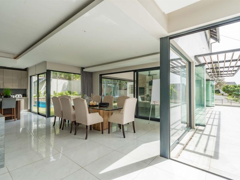 Modern open-plan living and dining area featuring large format floor tiles, recessed ceiling lighting, and seamless indoor-outdoor flow through expansive sliding glass doors.