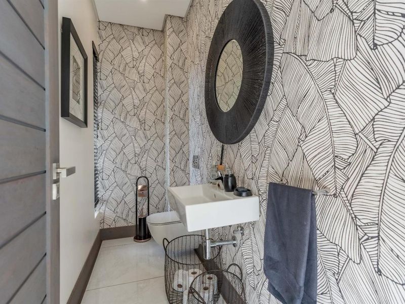 A modern guest cloakroom featuring a wall-mounted basin, toilet, and striking patterned wallpaper.