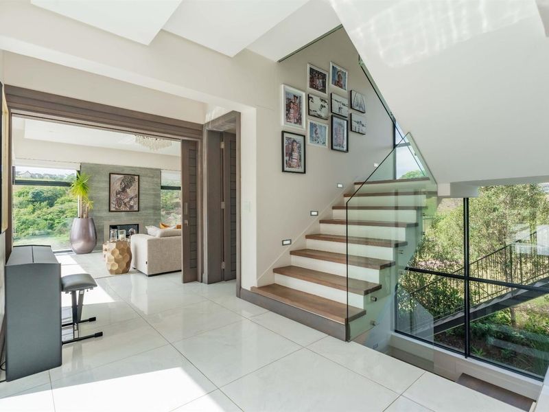 Modern entrance hallway featuring a sleek timber staircase with glass balustrade, polished porcelain flooring, and expansive windows overlooking the garden.