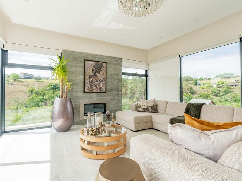 A bright and modern living room featuring a stone-clad built-in fireplace, expansive floor-to-ceiling windows with scenic views, and elegant recessed lighting.