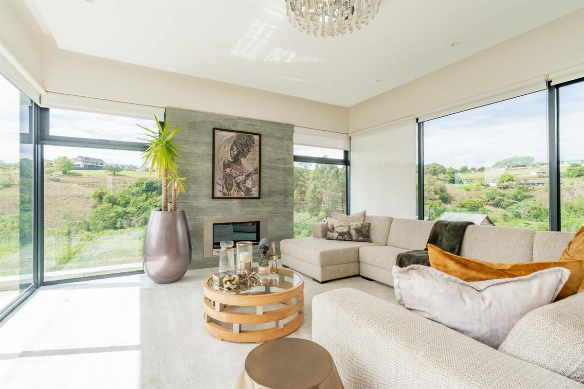 A bright and modern living room featuring a stone-clad built-in fireplace, expansive floor-to-ceiling windows with scenic views, and elegant recessed lighting.