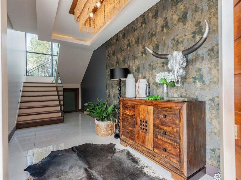 A modern, well-lit entrance hall featuring polished tiled floors, a striking feature wall, and a contemporary staircase with a glass balustrade.
