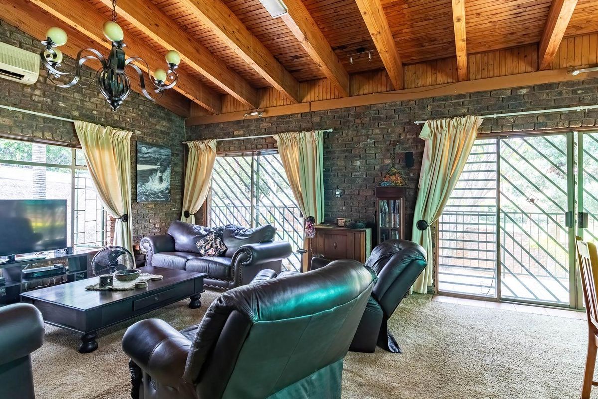 Spacious living room featuring exposed timber beam ceilings, rustic face-brick walls, and large sliding glass doors with security gates leading to the exterior.