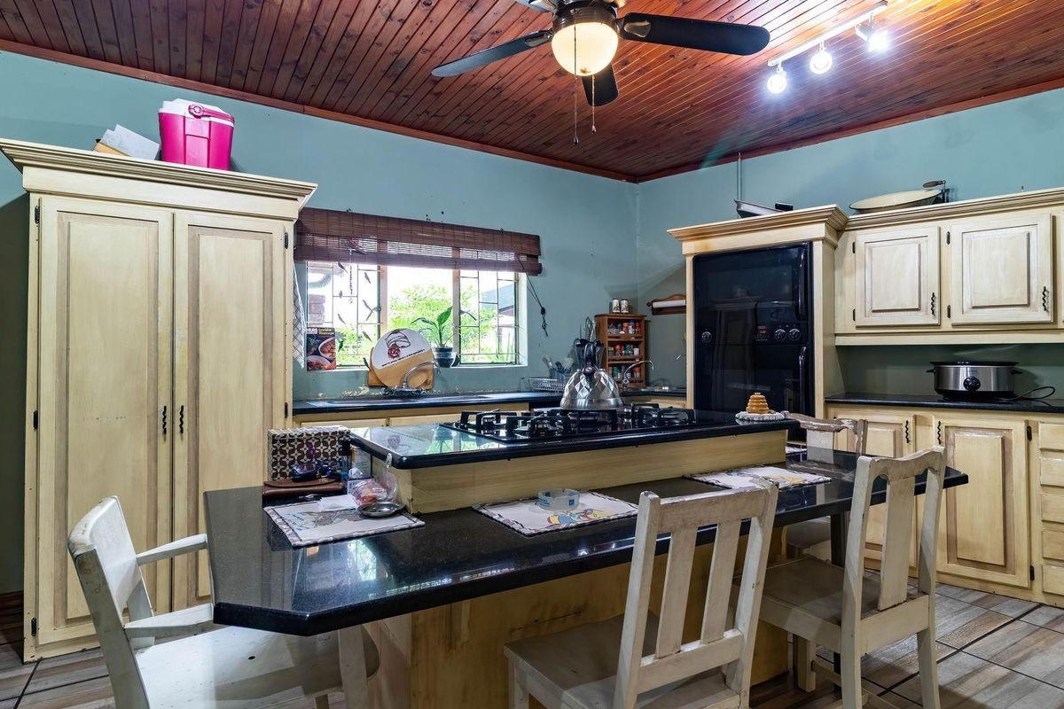 A traditional kitchen featuring a central island with a built-in gas hob, granite countertops, and timber cabinetry under a wood-paneled ceiling.